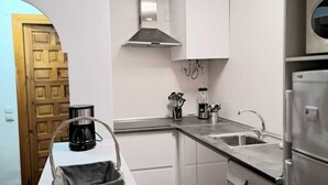 A compact kitchen with white cabinets, a built-in oven, a microwave, a coffee maker, and a washing machine. - Apartamento Junto al mar en Almuñécar, Recien Renovado y Equipado Para 4 pax (Almuñecar)