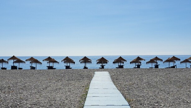 A pebble beach with rows of thatched umbrellas and tables, leading to the sea. - Apartamento Junto al mar en Almuñécar, Recien Renovado y Equipado Para 4 pax (Almuñecar)