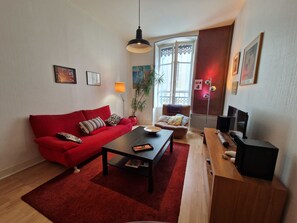 A living room with a red sofa, a coffee table, a TV stand, and a potted plant. - #GL | The Victor Hugo 🖼️|  T4 Hypercenter (Grenoble)