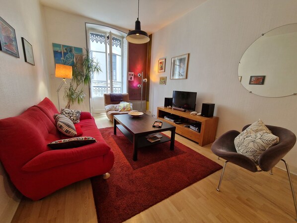 A living room with a red sofa, a coffee table, a TV on a wooden stand, and a plant. - #GL | The Victor Hugo 🖼️|  T4 Hypercenter (Grenoble)