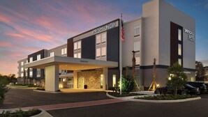 A modern hotel with a flat roof, a covered entrance, and a parking area.