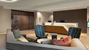 A modern reception area with a reception desk, seating area, and a large window with vertical blinds.