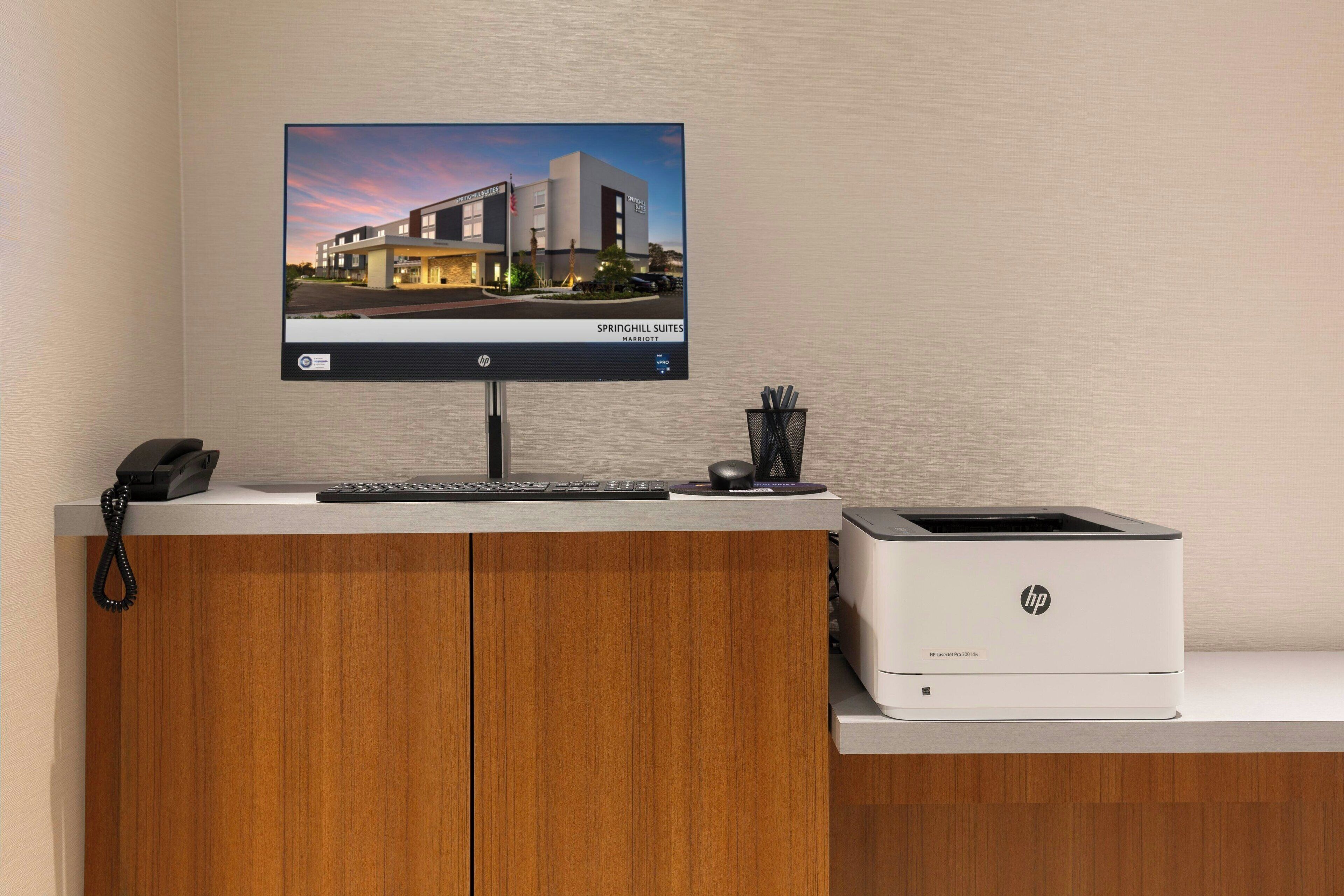 A hotel reception desk with a computer monitor displaying a building image, a telephone, a keyboard, a mouse, and an HP printer.