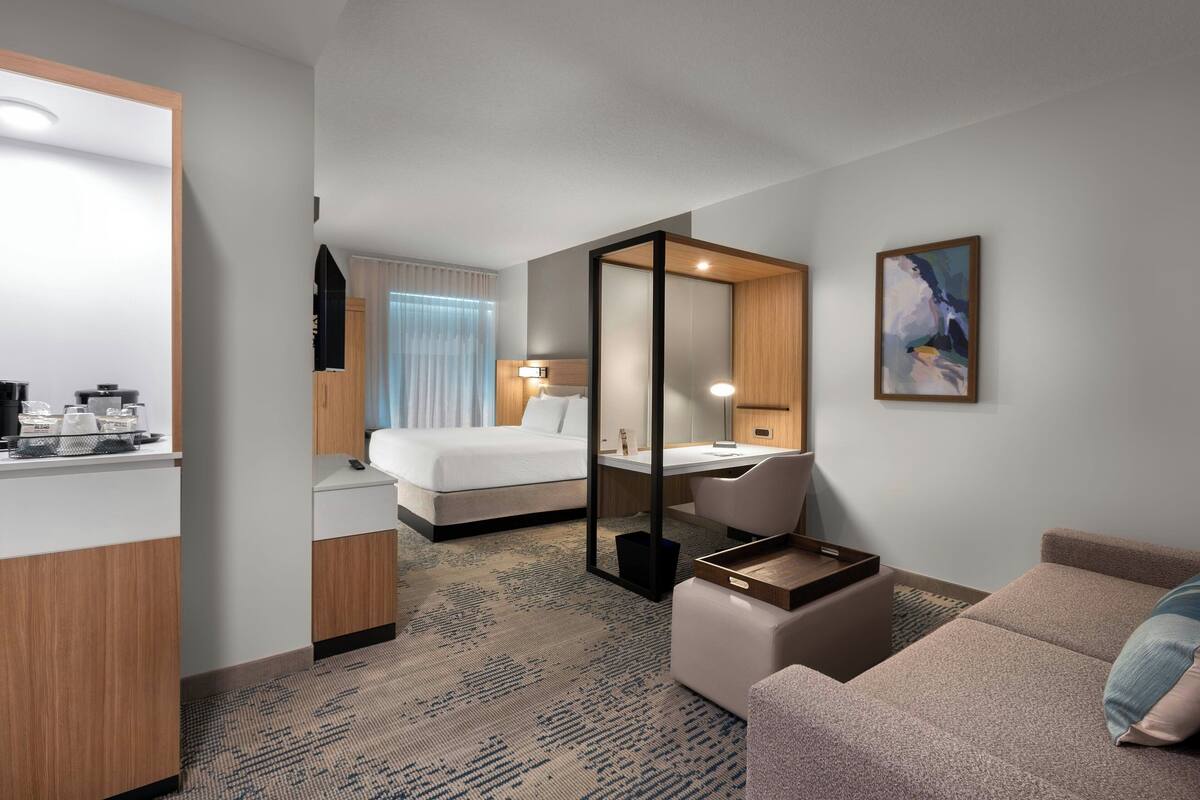 Une chambre d’hôtel avec un lit, un bureau, une chaise, un canapé, un miroir et un tableau au mur.