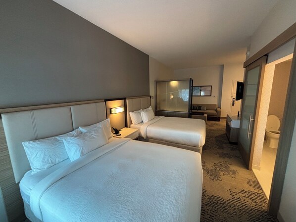 A hotel room with two beds, a bedside table with a lamp, a small sofa, a mirror, and a bathroom with a toilet and sink. - SpringHill Suites by Marriott West Melbourne Palm Bay (Melbourne)