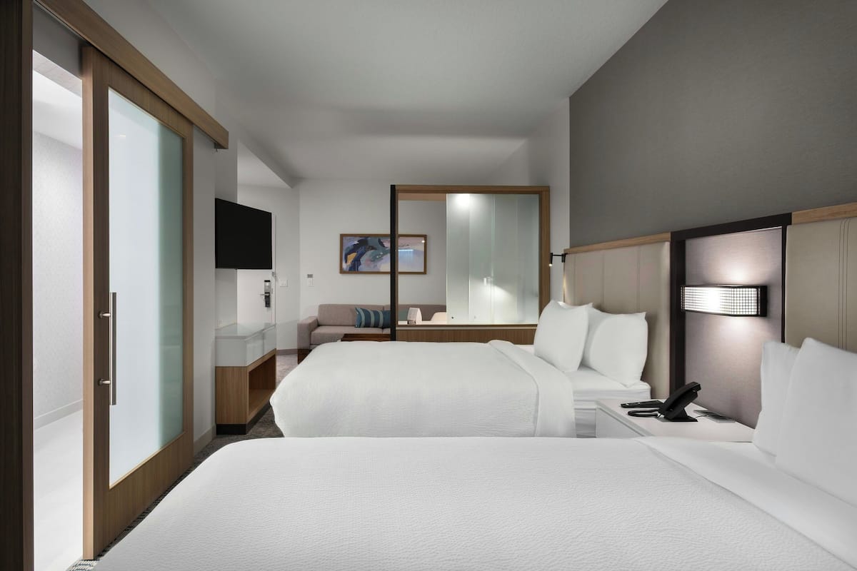 Une chambre d’hôtel avec deux lits, un téléviseur à écran plat, une table de chevet avec un téléphone, un miroir et un tableau au mur.