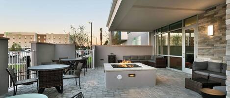 Un patio al aire libre con suelo de piedra, mobiliario de mimbre, una chimenea y una pared de acento de piedra.