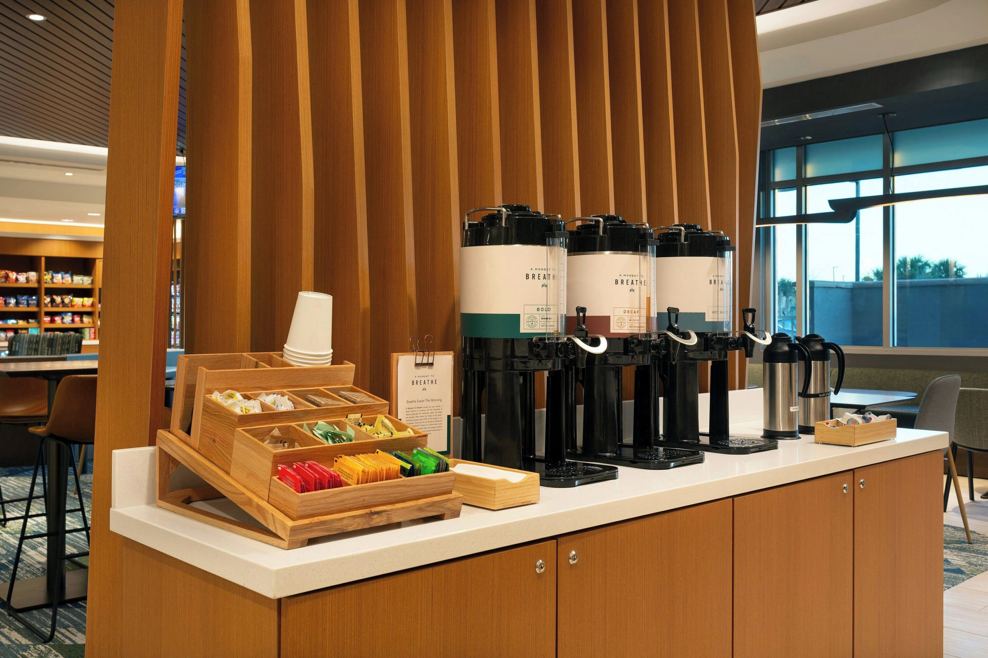 A coffee station with multiple coffee makers and a tray of assorted pastries.