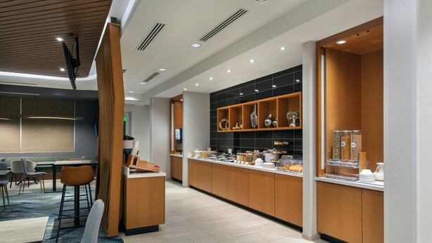 A modern kitchen area with wooden cabinets, a countertop with food items, and a seating area with chairs and a table.
