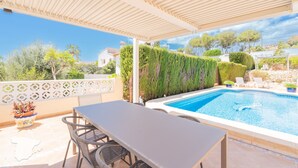 Ein überdachter Außenbereich mit Pool, Tisch und Stühlen.