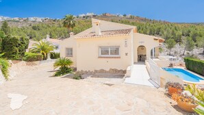 Ein Haus im mediterranen Stil mit einer Steinterrasse, einem Swimmingpool und Blick auf eine Hügelkuppe mit Häusern.