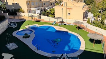A swimming pool with a 'Montesa Sol' logo, surrounded by lounge chairs and umbrellas, with a view of residential buildings and greenery.
