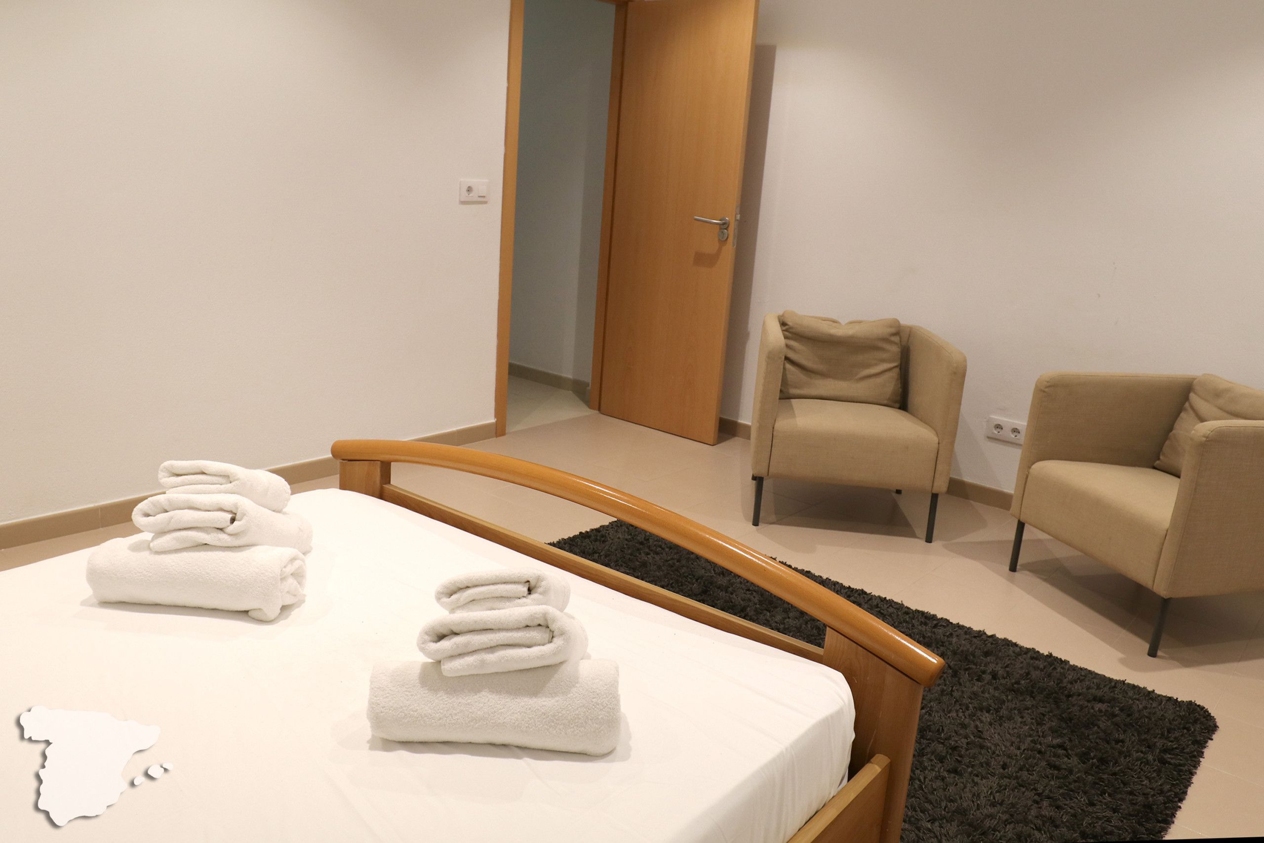 Une chambre à coucher avec un lit, deux chaises et une porte donnant sur une autre pièce.