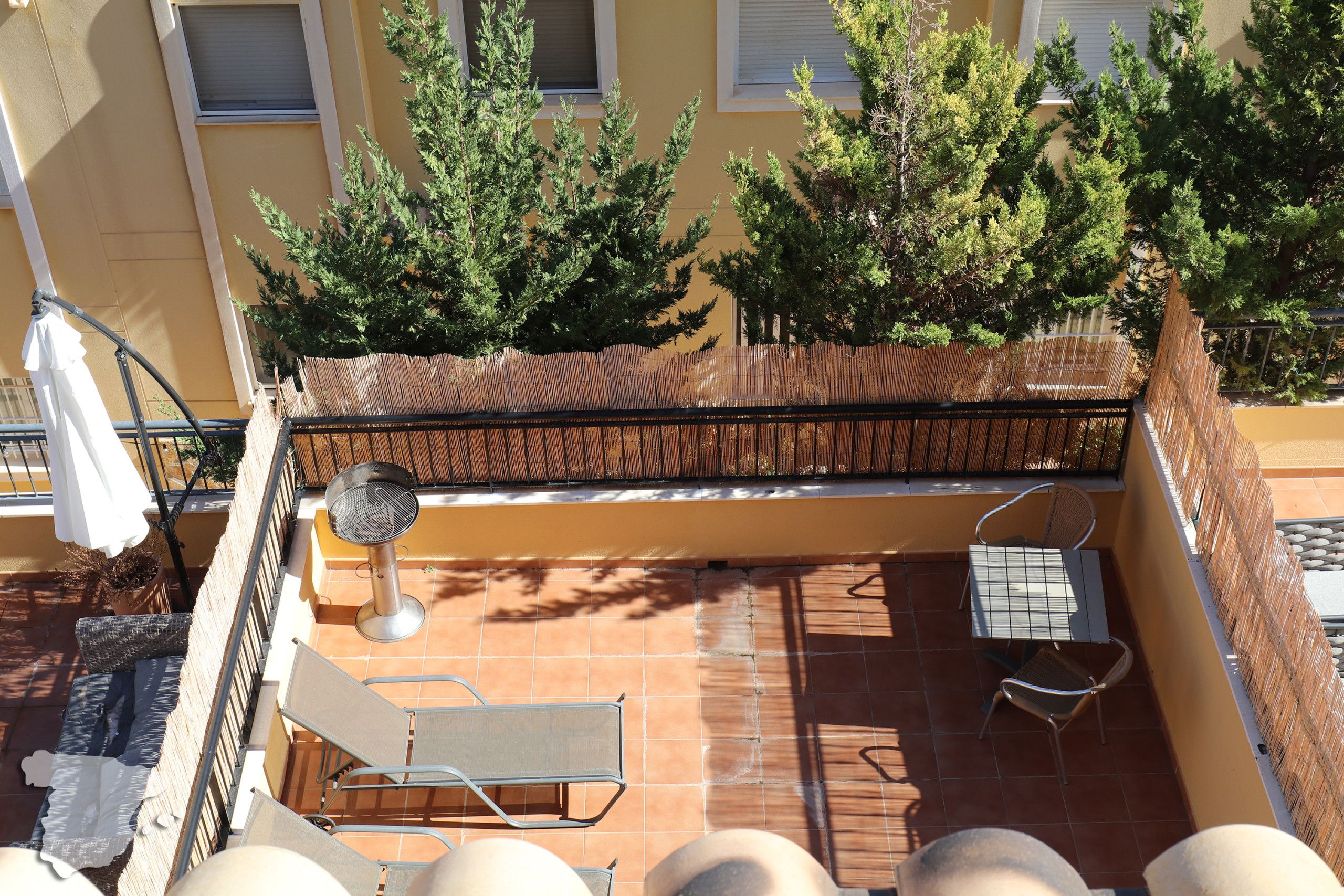 Een terras met een barbecue, stoelen en een tafel.