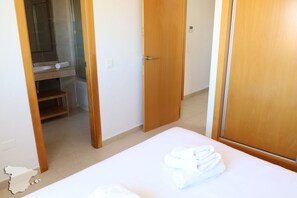 A hotel room with a bed, a wooden door, a bathroom with a sink, and a towel on the bed.