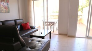 A living room with a black leather sofa, a red pillow, a coffee table, and a view of an outdoor patio with a table and chairs.