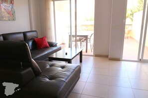 A living room with a black leather sofa, a red pillow, a coffee table, and a view of an outdoor patio with a table and chairs.