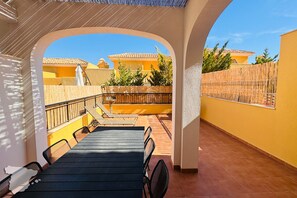 Un espacio al aire libre techado con mesa y sillas, vistas del barrio y una cerca de madera.