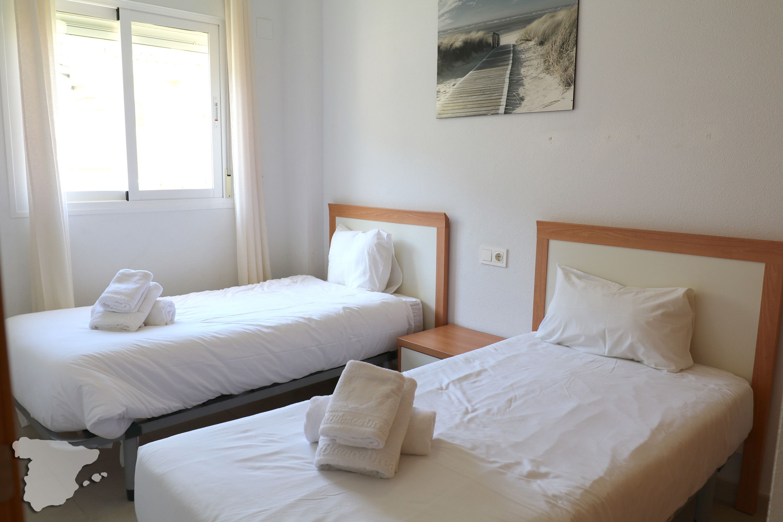 Hotellihuone, jossa on kaksi erillistä sänkyä. Jokaisessa sängyssä on puinen pääty, valkoiset vuodevaatteet ja rullalle taitettu pyyhe.