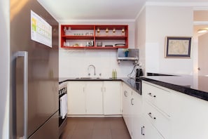 Una cocina moderna con armarios blancos, encimera negra y estante rojo con cristalería.