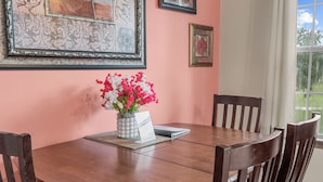 Une table à manger avec des chaises, un vase rempli de fleurs et des œuvres d’art encadrées accrochées au mur.