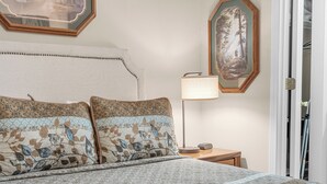 Un lit bien fait, avec une literie à motifs, une lampe de chevet et deux tableaux encadrés accrochés au mur.