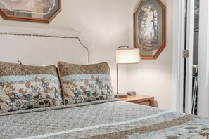 A neatly made bed with patterned bedding, a bedside lamp, and two framed pictures on the wall.