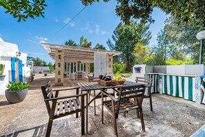An outdoor patio with wooden tables and chairs, a pergola, and a small garden area. - Trullo Nicolo With Pool Martina Franca (Martina Franca)