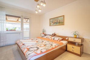 Een slaapkamer met een bed, nachtkastjes, gordijnen en een schilderij aan de muur.
