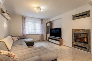 Een woonkamer met een bank, televisie, open haard en een raam met gordijnen.