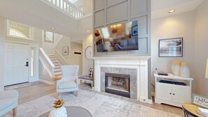 Un salón espacioso con chimenea, televisor montado encima y una escalera que sube a otro nivel.