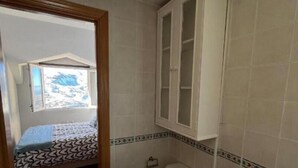 Une petite salle de bain comprenant des toilettes, un bidet et un meuble au-dessus des toilettes. Il y a une fenêtre donnant sur une maison à l’extérieur.