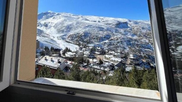 Une fenêtre donnant sur une montagne enneigée et sur une ville située en contrebas.