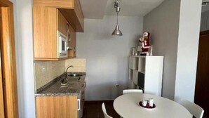 Une cuisine compacte dotée de meubles en bois, d’un four à micro-ondes encastré et d’un coin repas avec une table ronde et quatre chaises.