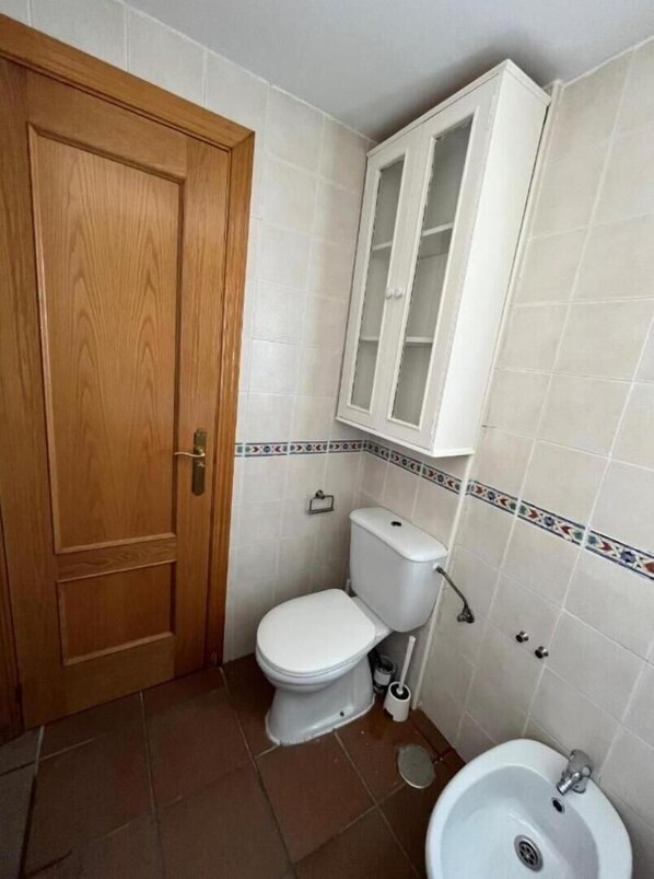 A small bathroom with a wooden door, a toilet, a sink, and a cabinet above the toilet.