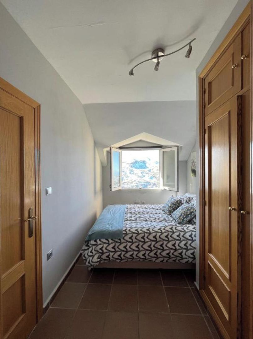 A narrow room with a bed, wooden wardrobe, and a sloped ceiling with a light fixture.