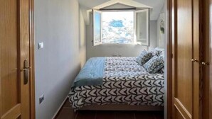 Une petite pièce avec un lit, une armoire en bois et un plafond en pente agrémenté d’un luminaire.