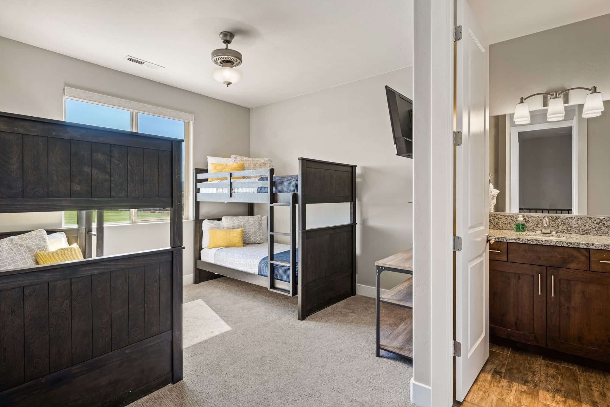 A room with bunk beds, a small table, a mirror, and a window.