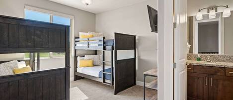 A room with bunk beds, a small table, a mirror, and a window.