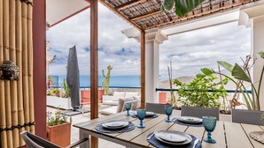 Un patio con una mesa lista para comer, con vista a una playa y el océano.