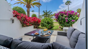 A patio with outdoor furniture, a table with breakfast items, and lush greenery including pink bougainvillea and palm trees. - Luxury apartment on the beach (La Caleta)