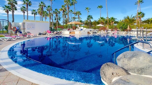 A swimming pool surrounded by lounge chairs and palm trees. - Luxury apartment on the beach (La Caleta)