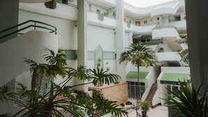 A multi-level atrium with a central staircase, surrounded by palm trees and a Costa Caleta sign. - Luxury apartment on the beach (La Caleta)