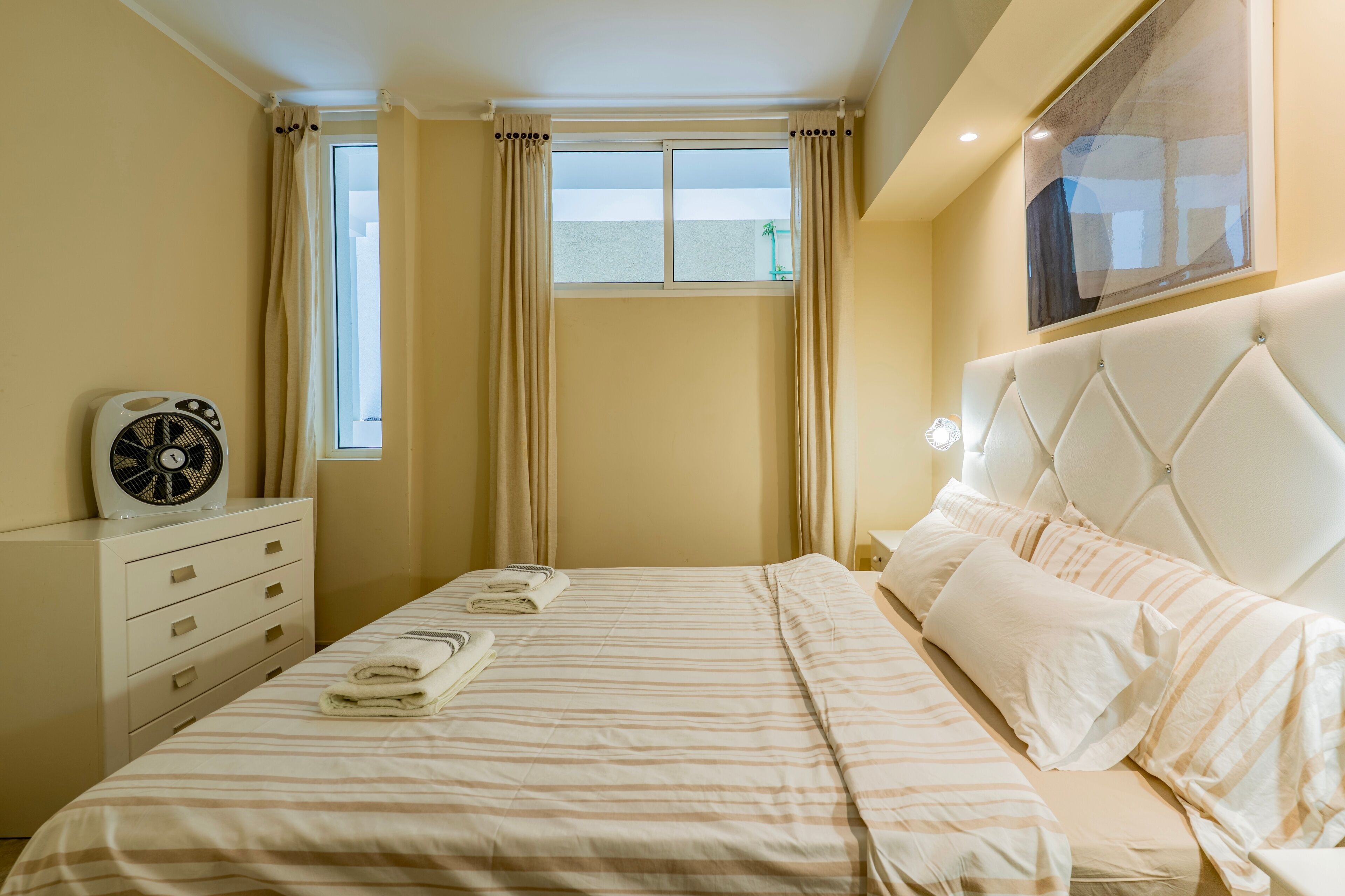 Quarto bem organizado com cama, mesa de cabeceira e janela com cortinas.