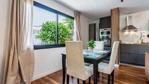 A modern kitchen with built-in appliances, a dining area with a glass table and chairs, and a view of greenery outside. - Centric and bright apartment - Puerto de La Cruz (Puerto de la Cruz)