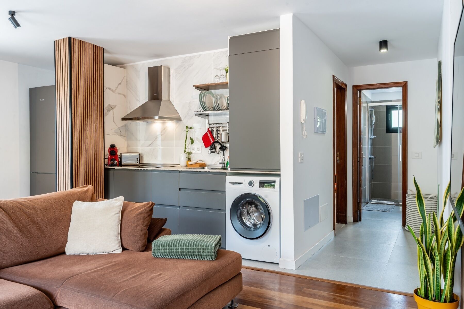 A modern kitchen with a built-in washing machine, grey cabinets, and a wooden accent wall.