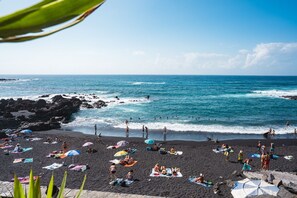 Una playa con gente tomando el sol y nadando, costa rocosa y mar azul cristalino.