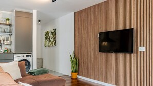 A modern living room with a flat-screen TV mounted on a wooden wall, a sofa, a washing machine, and a potted plant. - Centric and bright apartment - Puerto de La Cruz (Puerto de la Cruz)
