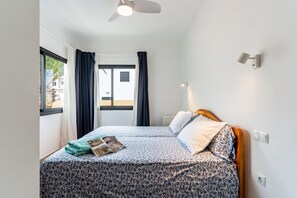 Un dormitorio con cama, cortinas, ventilador de techo y ventana con vistas al exterior.