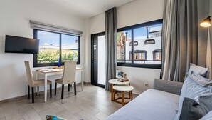A modern hotel room with a bed, a desk with chairs, a small table, and a TV.
